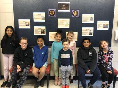 Group of elementary students pose for photo in front of hallway board