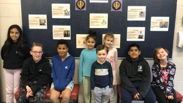 Group of elementary students pose for photo in front of hallway board