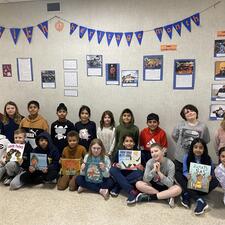Group of elementary students pose for photo in front of decorated board